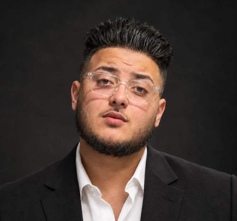 Mohammed Alajnaf, a young man with dark hair and a beard, standing against a dark wall.